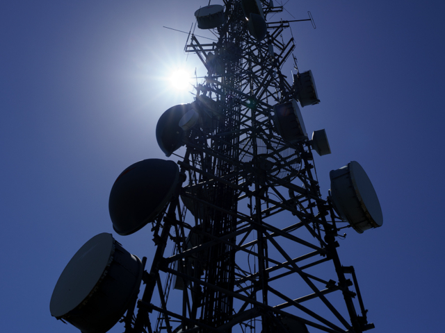 A communication tower reaches into the sky as the sun shines down